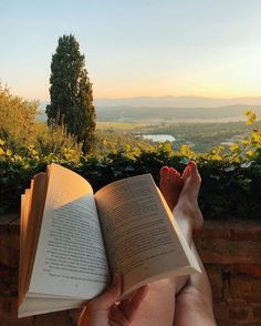 someone is reading a book while sitting on a ledge