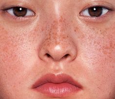 a woman with freckles on her face is looking at the camera while she has brown eyes