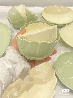 a person holding a green bowl in front of several plates on a white tablecloth