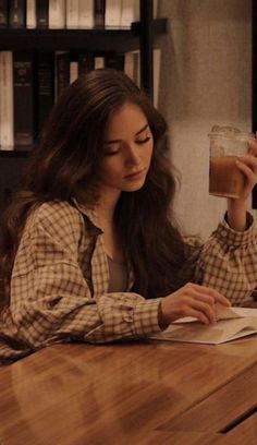 a woman sitting at a table with a book and glass in her hand, looking down