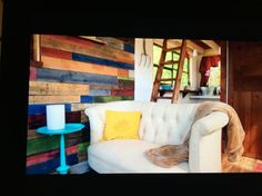 a white couch sitting in front of a wooden wall covered in multicolored wood planks