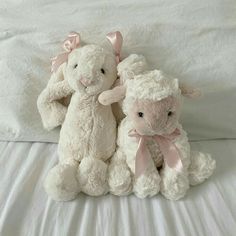 two stuffed animals sitting on top of a bed next to each other with pink bows