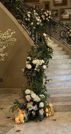 flowers and candles are on the floor next to an ornate stair case with white roses