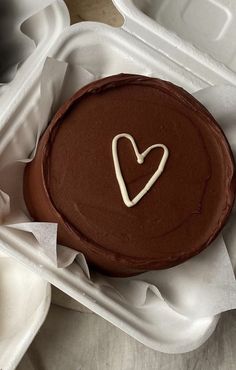 a chocolate cake with a heart on top in a white take - out container, ready to be eaten