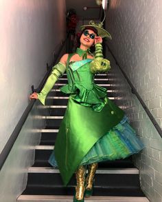 a woman dressed in green is walking down the stairs