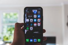 a person holding up an iphone with icons on the screen and in front of a tv