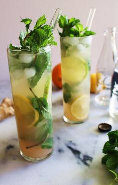 two tall glasses filled with lemonade and mint mojito cocktails on a marble table