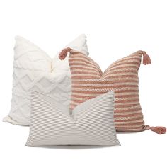 three pillows with tassels on them, one in orange and the other in white