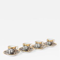 four coffee cups and saucers with gold trimmings on them, set against a white background