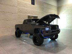 a gray truck with its hood open in a room filled with white walls and concrete flooring