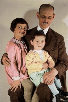 an old photo of a man and woman with a baby in their lap, smiling at the camera