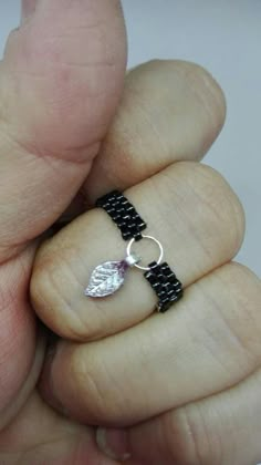 a hand holding a black and silver bracelet with a leaf charm