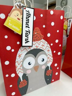 a red shopping bag with an image of a penguin on it and some tags hanging from the handles