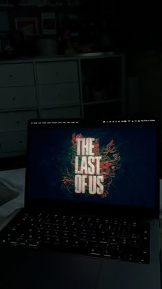 an open laptop computer sitting on top of a bed in a dark room with the words the last of us written on it