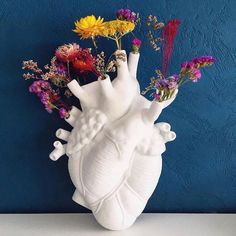 a heart shaped vase with flowers in it on a table next to a blue wall