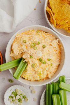 two bowls filled with dip and celery next to some tortilla chips