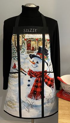 a snowman is wearing a red scarf and black shirt with the words suzzie on it