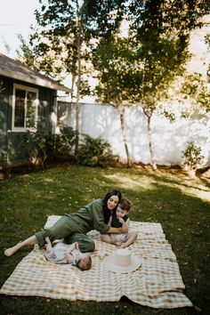 a woman laying on top of a blanket next to two babys in the grass