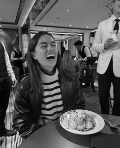 a woman laughing while sitting at a table in front of a plate with food on it