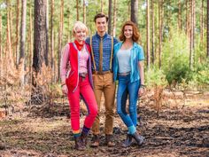 three people standing next to each other in the woods