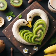 sliced kiwi fruit in the shape of a heart on a cutting board next to bananas and other fruits