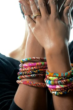 a woman holding her hands up to her face with colorful bracelets on her wrist