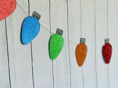 christmas lights are hanging on a string against a white wall with red, green and blue tinsel