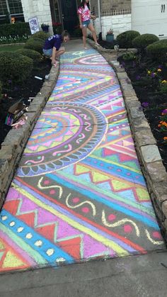 two children are drawing on the sidewalk in front of a house with colorful chalk paint