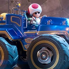 a blue toy truck with two large wheels and a man riding in the back seat