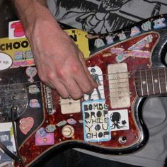 a close up of a person playing an electric guitar with stickers on the body