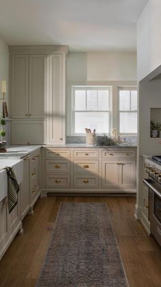 a kitchen with white cabinets and wooden floors, an area rug in the middle of the floor