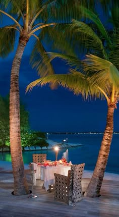 an outdoor dining area with palm trees and the ocean in the background at night time