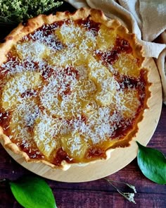 an uncooked pizza with cheese and sauce on a wooden plate next to some green leaves