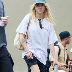 a woman walking down the street with a water bottle in her hand and wearing a hat