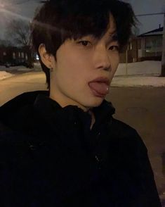 a young man sticking out his tongue on the street at night time with snow and houses in the background