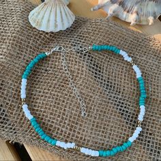 a blue and white beaded bracelet sitting on top of a table next to a seashell