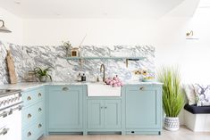 a kitchen with marble counter tops and blue cabinets, along with potted plants in the corner