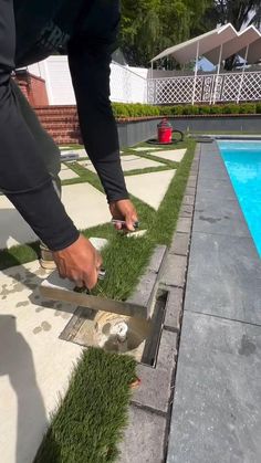 a person cutting grass with scissors near a swimming pool