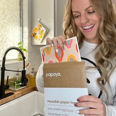 a woman holding up a paper towel in her hands and smiling at the camera while standing next to a kitchen sink