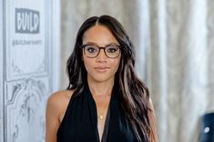 a woman wearing glasses standing in front of a wall with an advertisement on it's side