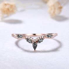 a rose gold ring with two pear shaped diamonds on the top and side, sitting on a white surface