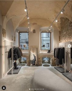 the inside of a clothing store with lots of clothes hanging on racks and windows in it