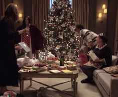 people are gathered around a christmas tree in the living room with presents on the coffee table