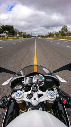 a motorcycle driving down the middle of an empty road with yellow lines on both sides