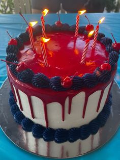 a birthday cake with red and white frosting, lit candles on top is sitting on a blue tablecloth