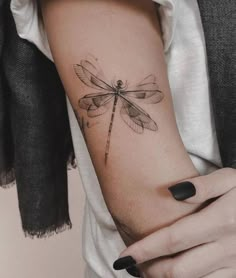 a woman's arm with a dragonfly tattoo on the left side of her arm