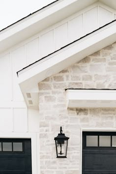 two black garage doors and a light on the side of a white brick building with windows