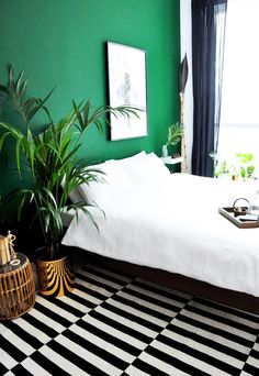 a bedroom with green walls and black and white checkered flooring, potted plants in front of the bed