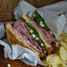 a sandwich with meat, cheese and lettuce next to chips on a table