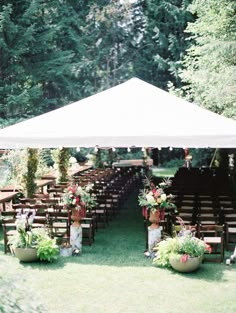 an outdoor ceremony setup with chairs and flowers on the grass under a white awning